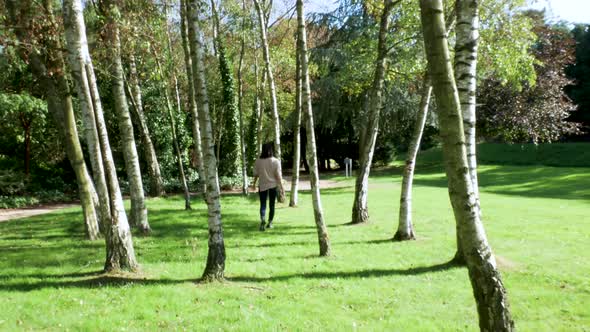 Woman walking between silver birch trees in lush surroundings.