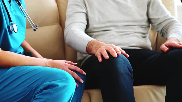 Close Up Shot of Female Nurse Taking an Old Man Hand While They Are Sitting on the Couch