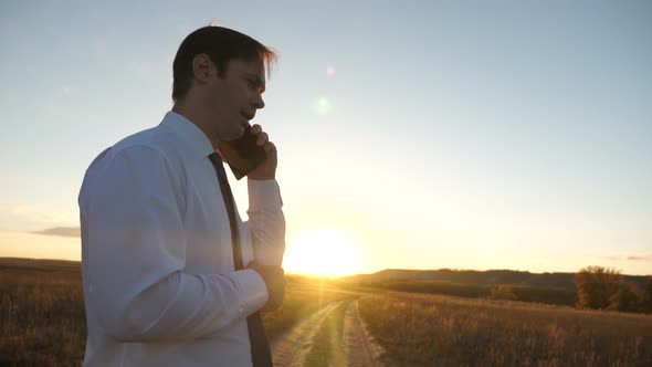 Businessman Talking on a Smartphone Against the Sky. Man in a Tie with a Tablet in the Park