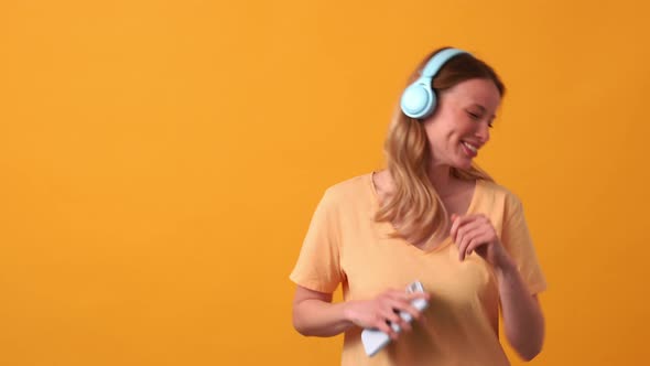 Pleased blonde woman wearing yellow t-shirt listening music in headphones