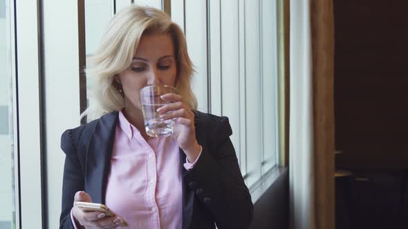 Business Woman Drinks Water and Looks at Photos in Her Phone