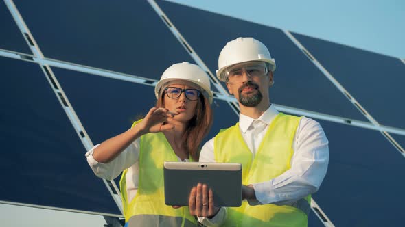 Two Technicians Are Discussing Construction Project with a Solar Installation Behind Them