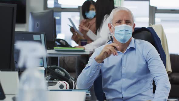 Portrait of man wearing face mask sitting on his desk in office