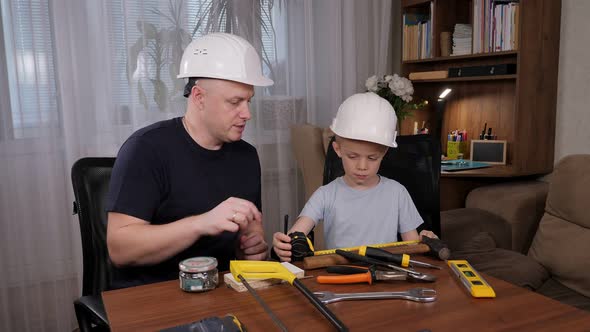 Handsome Bald Man Showing Instruments to His Son While Sitting at the Table