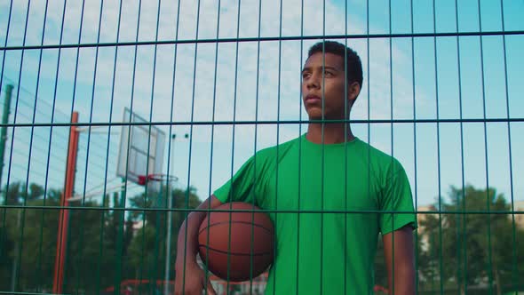 Pensive Basketball Player Holding Ball in Urban Court