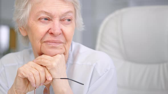 Senior lady pensioner holds head on wrinkly hands with glasses