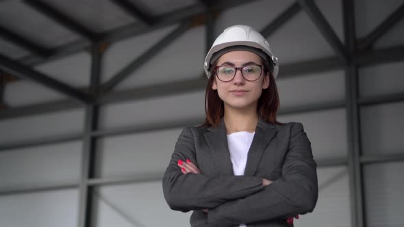 A Young Woman in a Protective Helmet Crossed Her Arms and Stands at a Construction Site. The Boss