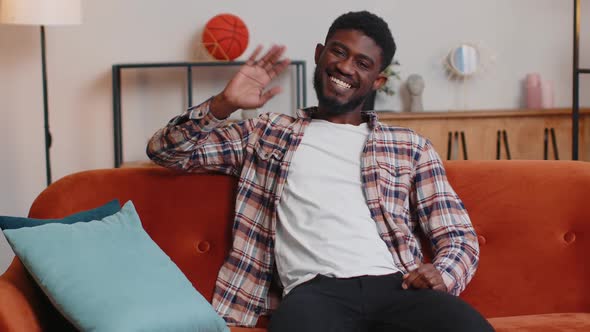 Young Man Smiling Friendly at Camera Waving Hands Gesturing Hello Hi Greeting at Home on Sofa