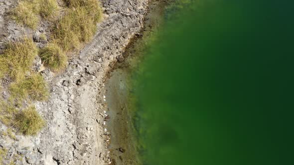 An almost chemical green colored lake with a rocky beach seen from above