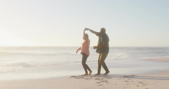 Smiling senior african american couple holding hands and dancing on sunny beach