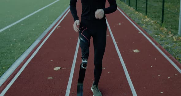 Disabled Male Sportsman with Amputated Leg with Prosthetic Blade Jogging at Sports Field