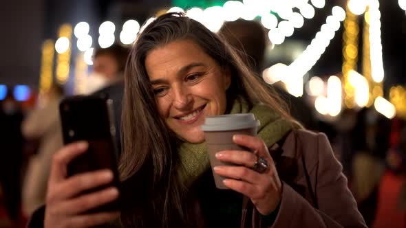 Happy female with takeaway coffee taking selfie on night street