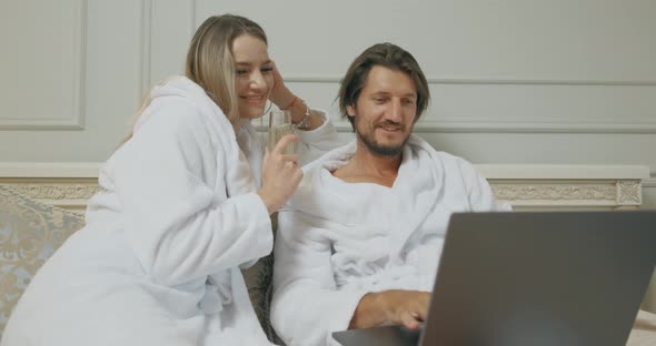 Young Tourists Couple Are Browsing the Internet at Laptop Together Sitting on a Bed in a Hotel Room