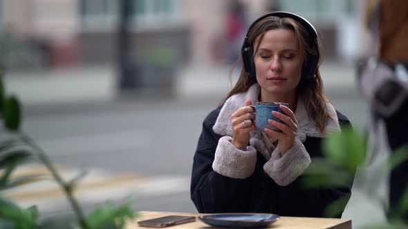 Portrait of a Young Woman Listening To Music with Headphones and Enjoying Sitting in an Outdoor Cafe