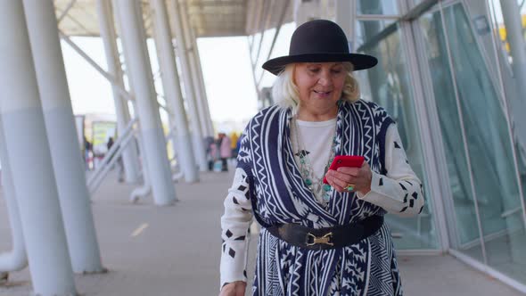 Senior Tourist Grandmother Woman Walking on International Airport Hall Using Mobile Phone Texting