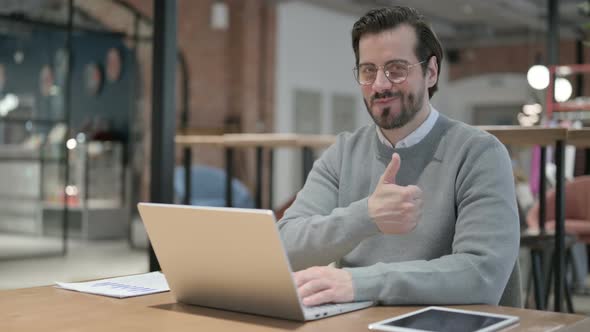 Young Man Showing Thumbs Up Sign While Using Laptop at Work