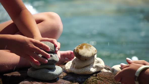 Woman Bilds Stones Pyramid on the Seashore on a Sunny Day on the Blue Sea Background