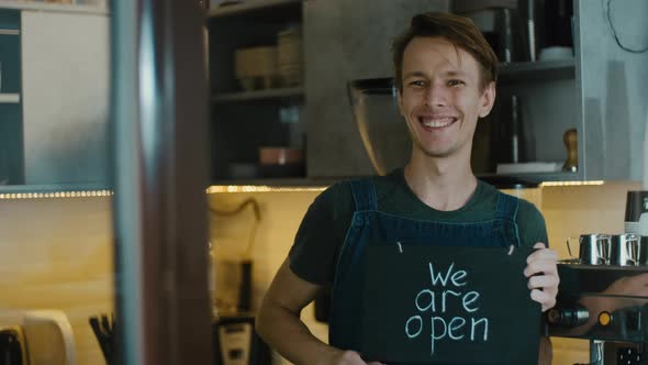 coffee shop owner invites new guests holding board with sign we are open after finishing quarantine