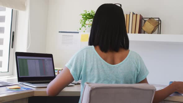 Mixed race gender fluid person sitting at desk drinking coffee working from home using a laptop