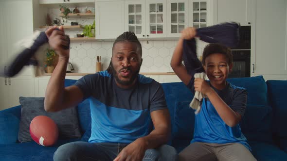 Excited Black Family of American Football Fans with Scarves Cheering Team Indoor