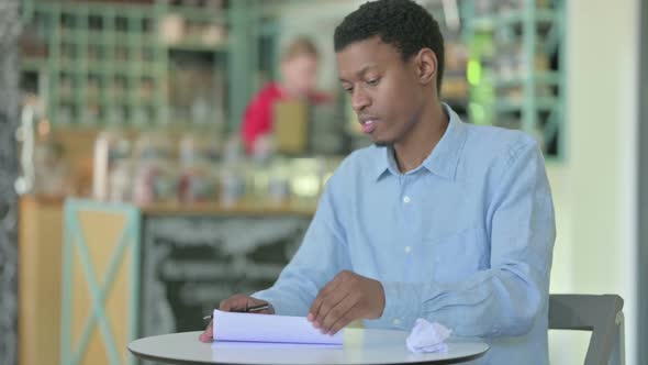 Disappointed Young African Man Trying to Write on Paper