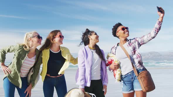 Happy group of diverse female friends having fun, taking selfie with smartphone at the beach