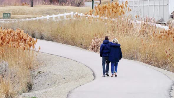 A couple with their arms around each other walking away (from behind) along a rural nature trail - s