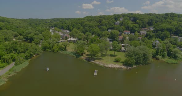 Flying Over Anchored Boats on Harbor and Towards Houses Amongst Trees