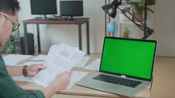 Designer Works On A Storyboard, Looks At His Sketches With Mock Up Green Screen Laptop