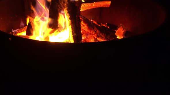 Campfire flames burn firewood bright orange during night at outdoor campsite.