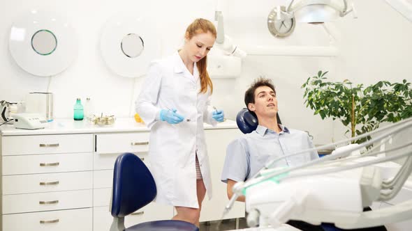 Female Dentist Examining Teeth of Young Man with Mirror During Dental Checkup in Medical Clinic