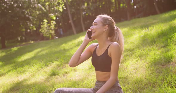 Happy Blonde Woman Talking on Mobile Phone, Sitting in Summer Par on Grass