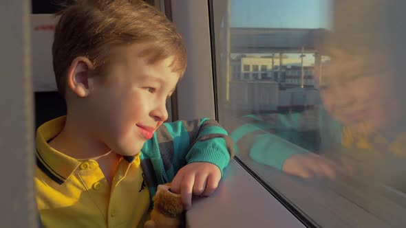 Little Boy Looks Out the Train Window and Holds a Toy