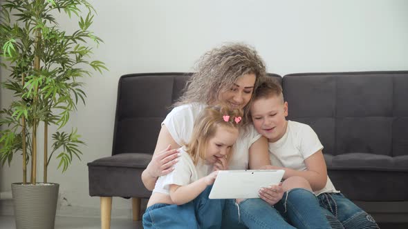 Mom and Daughter and Son Play with the Tablet in a Cozy Living Room