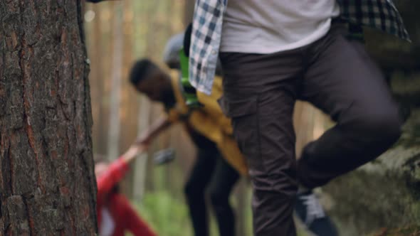 Multiethnic Group of Travelers Is Trekking Up Huge Rocks in Forest Carrying Heavy Backpacks, Men Are