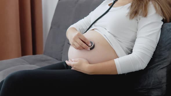 A Pregnant Woman Listens to the Movements and Heartbeat of the Fetus with a Stethoscope
