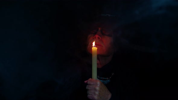 Sinister Old Mature Man in Carnival Costume of Halloween Witcher Making Magic Rituals with Candle