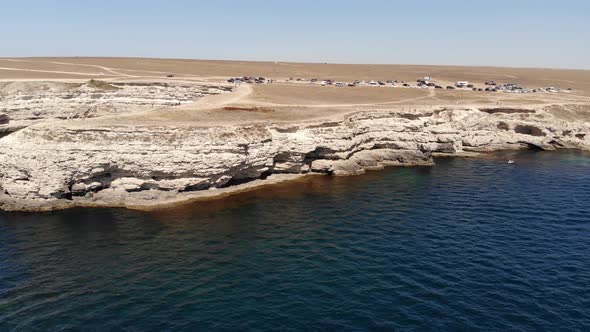 Aerial View of a Flight Near a Rocky Cape Under Which Tourist Boats Sail