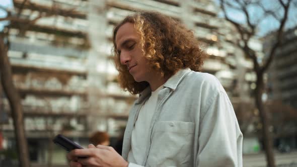Pretty curly-haired man looking at mobile while walking