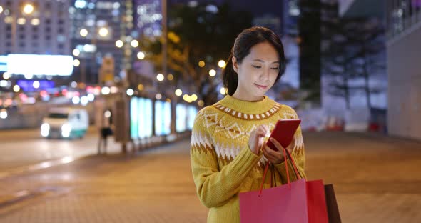 Woman holding with shopping bag and use of mobile phone in city at night