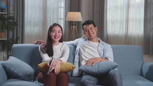 Happy Young Asian Couple Relaxing And Watching Tv At Home