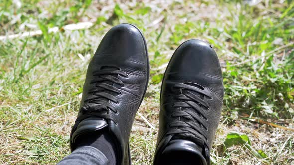 Closeup Feet of a Resting Tourist in Black Shoes on Green Grass on Nature