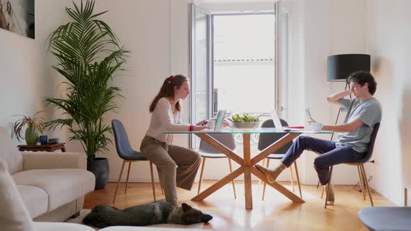 Young couple sitting at dining table using laptop and smartphone