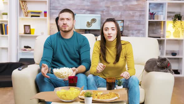 Excited Couple Sitting on the Couch Eating Junk Food