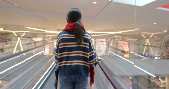 Woman taking escalator inside shopping mall