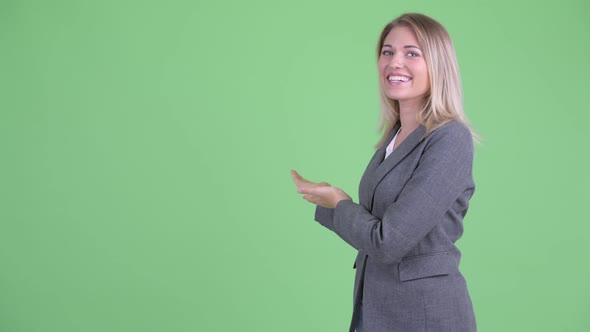 Happy Young Blonde Businesswoman Talking While Showing To the Back