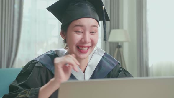 Asian Woman Wearing A Graduation Gown And Cap Having Video Call In Living Room