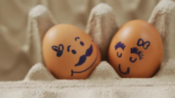 Video of close up of two brown eggs with drawn faces in egg carton background