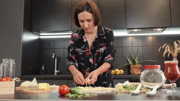 Woman lays grated cheese on base of pizza with tomato paste