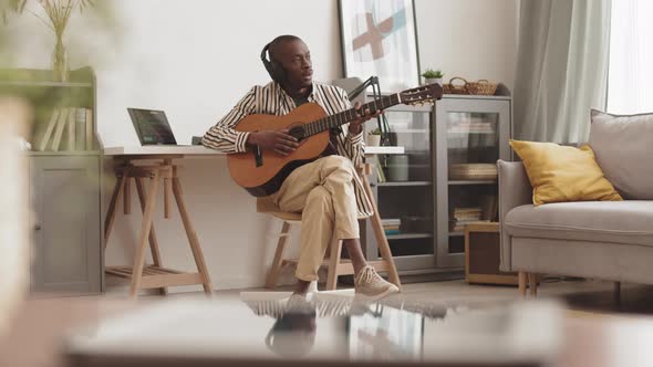 Artist Wearing Headphones Playing Acoustic Guitar at Home